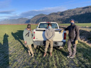 Three people stand near pickup truck in a field.
