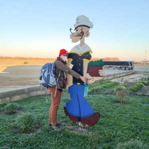 Woman wearing backpack hugs large plywood Popeye figure.