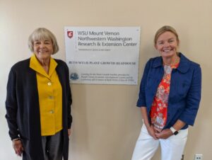 Two women pose with sign dedicating the Ruth Wylie Plant Growth Headhouse.