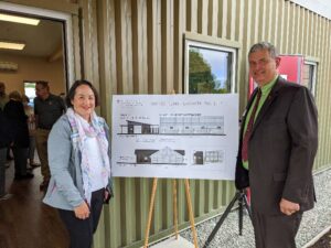 Two people pose next to architectural drawing on an easel.