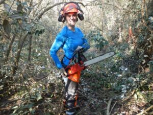 Woman with a chainsaw in a forested area.