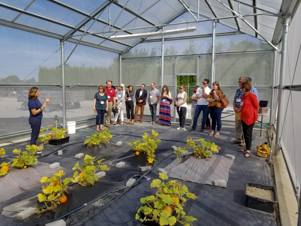 Woman speaks to group looking at pumpkin plants in a screenhouse.
