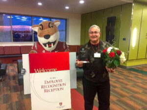 Juan Alonso poses with his length of service award next to a cardboard stand-up of Butch T. Cougar.