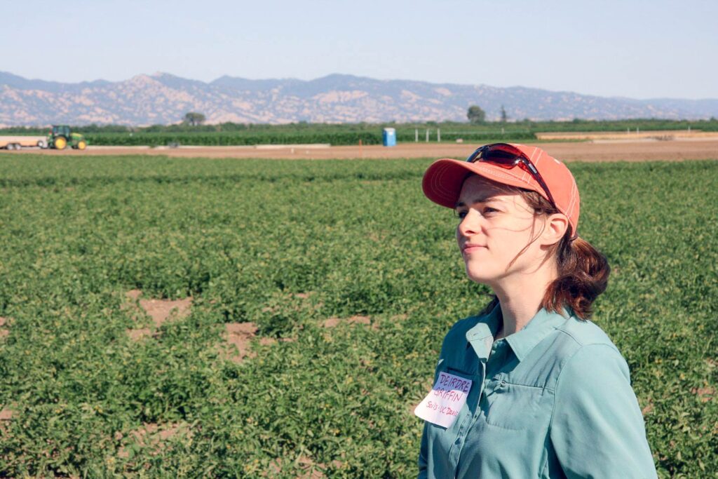 Deidre Griffin gazes out of frame with agricultural fields behind her.