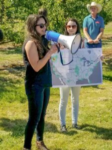 presenting with a megaphone next to an orchard.