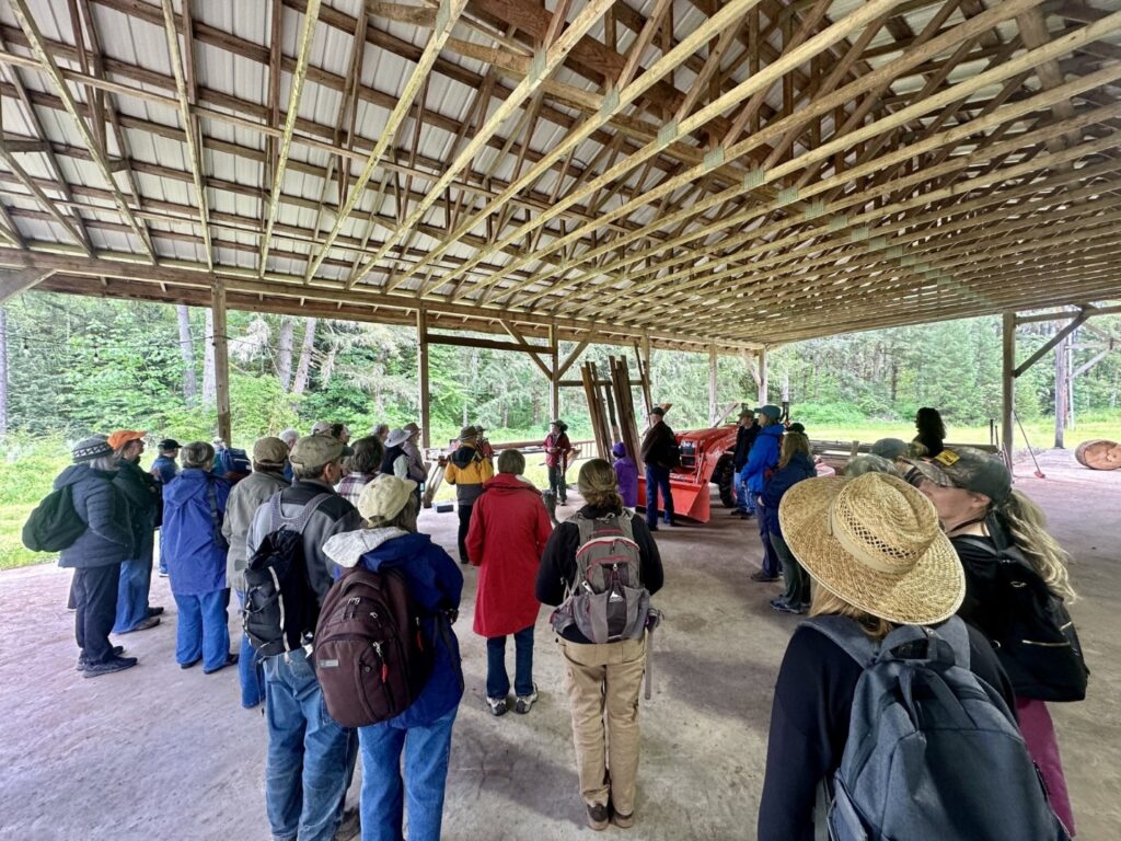 A large group of people listening to a speaker in an open-sided structure.