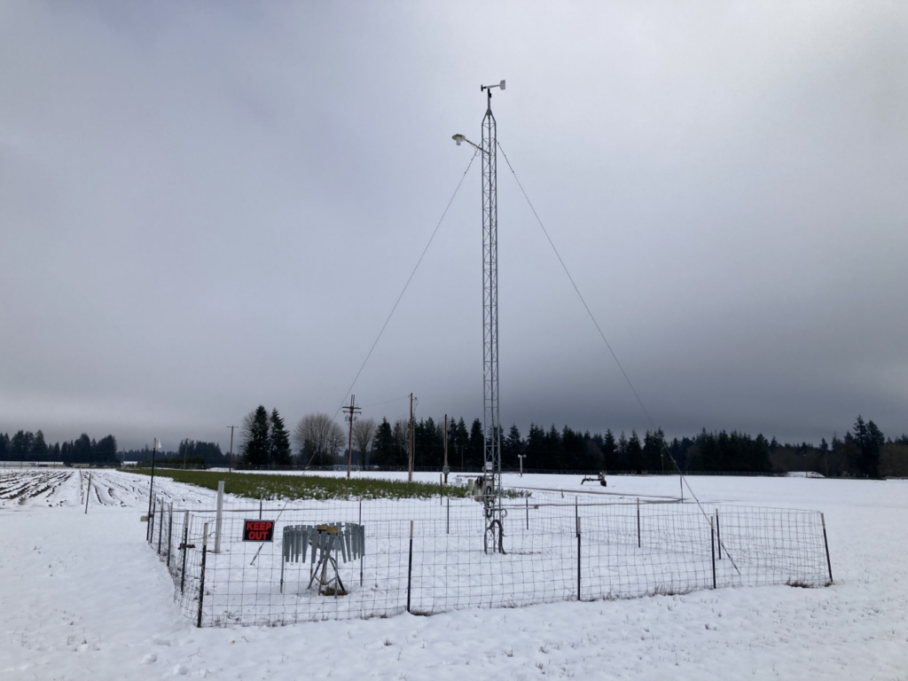 A tower supporting meteorology instruments in a snowy field.