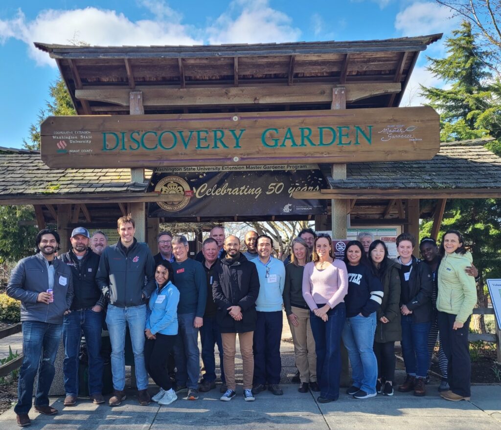 A large group of people stand under an entry arch reading 'Discovery Garden'.
