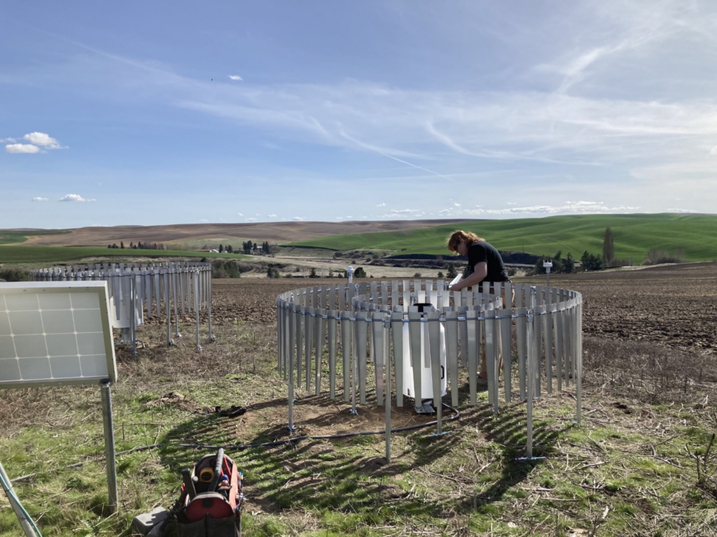 A woman works on a circular apparatus constructed of metal stakes.