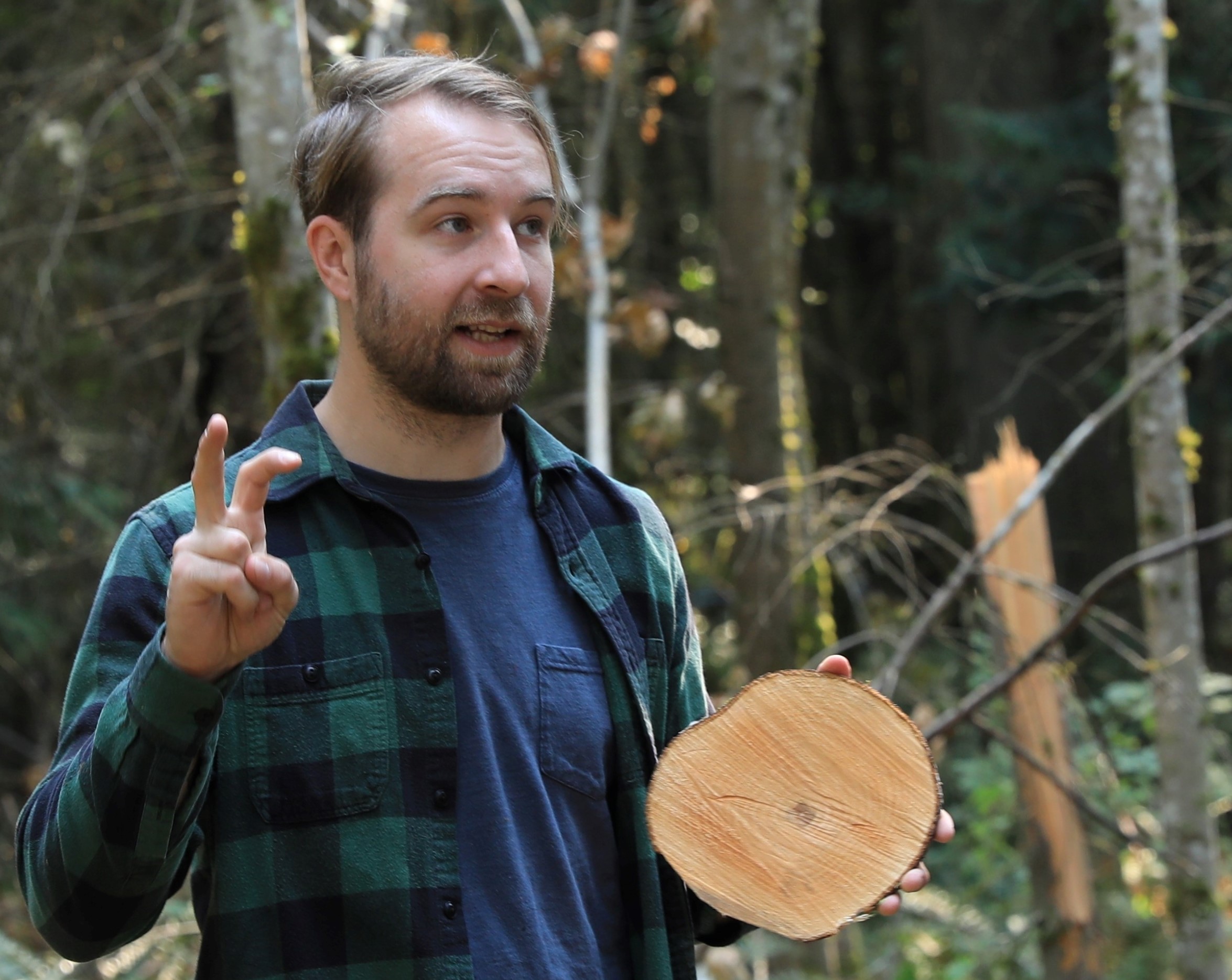 Bearded man holding a cross-section of a log.