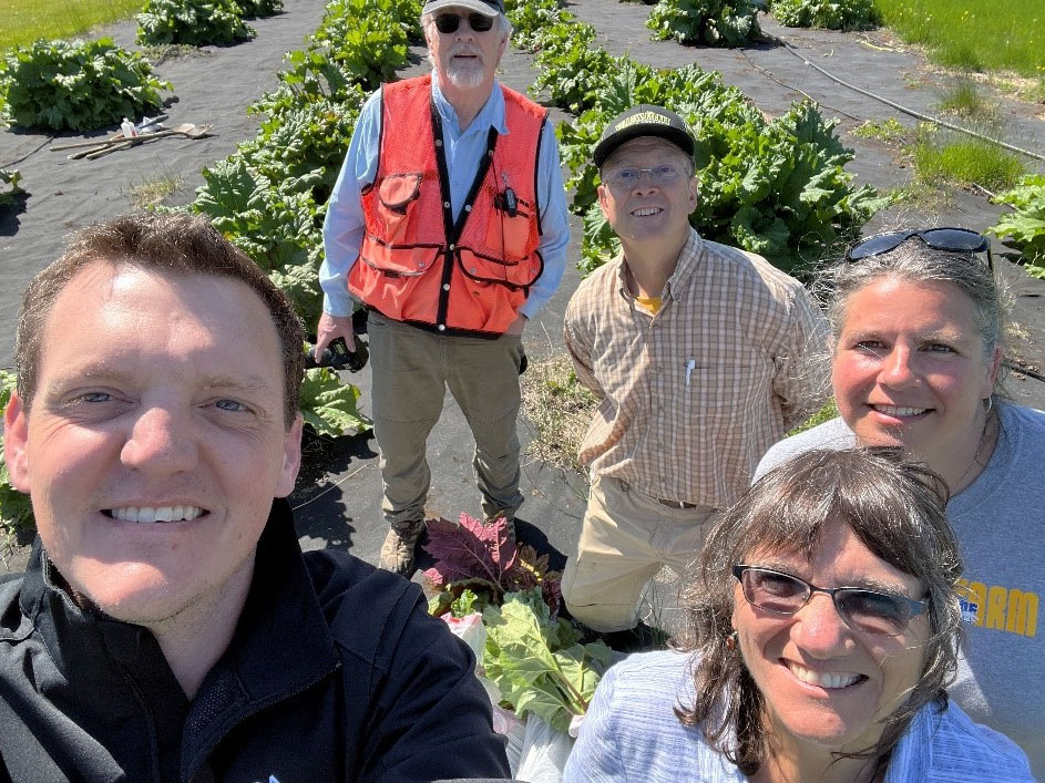 A group of people smiling for a photo in a rhubarb field in bright sunshine.