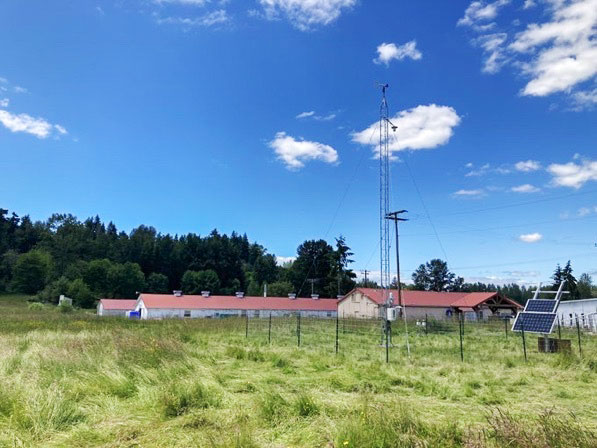 An antenna, sensors, and solar panels in front of a large barn and building complex.