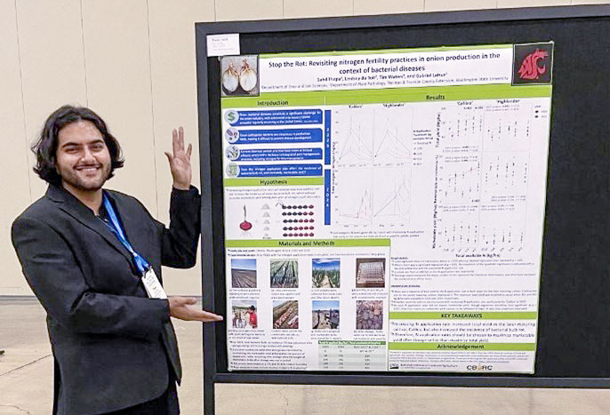 A man in a suit jacket motioning to a poster displayed next to him in a conference room.