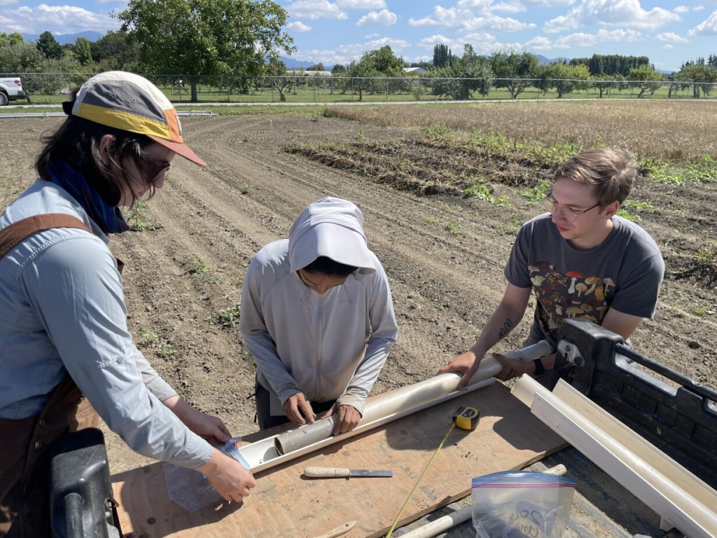 Three people holding metal a metal cylinder  in a field.