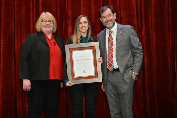 A woman holding a framed certificate, standing between a woman and a man.