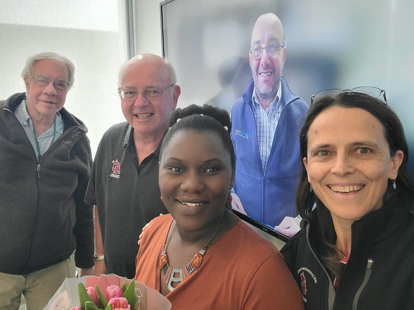 A group of people smiling for the camera, the woman in front is holding tulips.