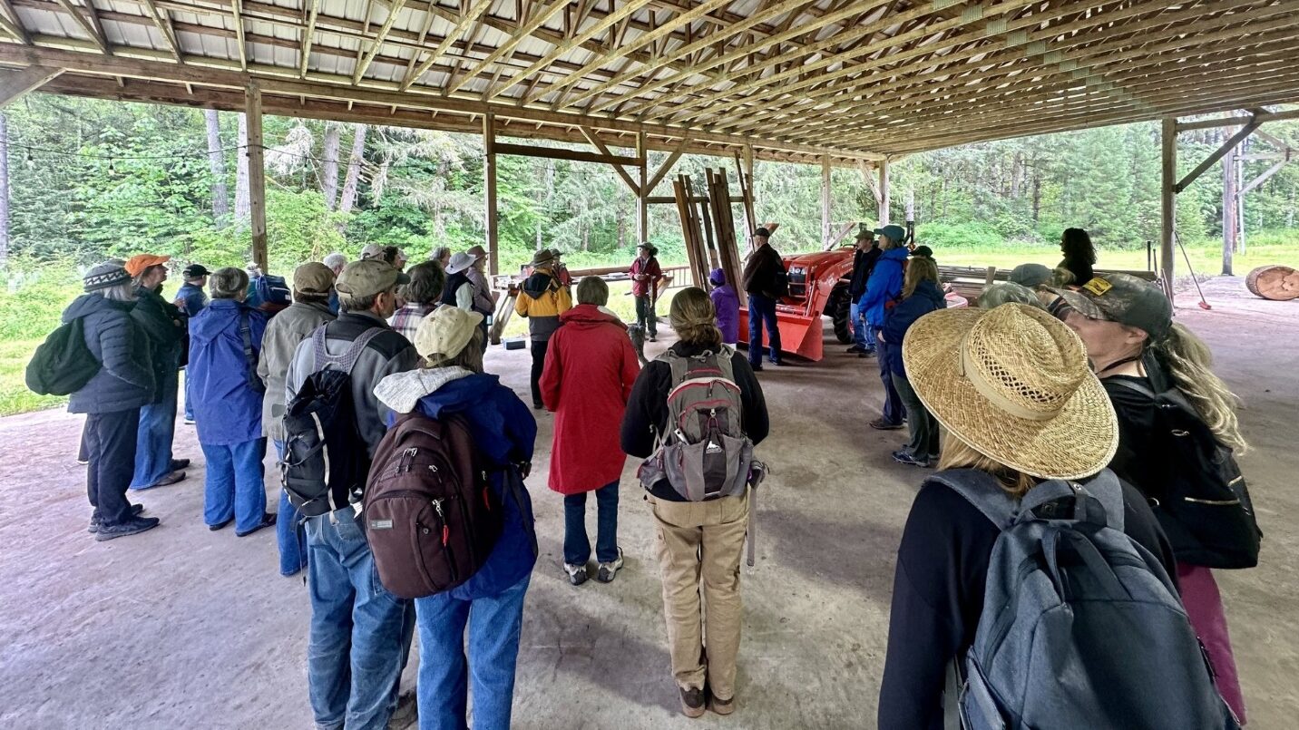 A large group of people listening to a speaker in an open-sided structure.