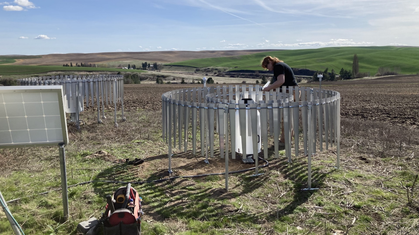 A woman works on a circular apparatus constructed of metal stakes.