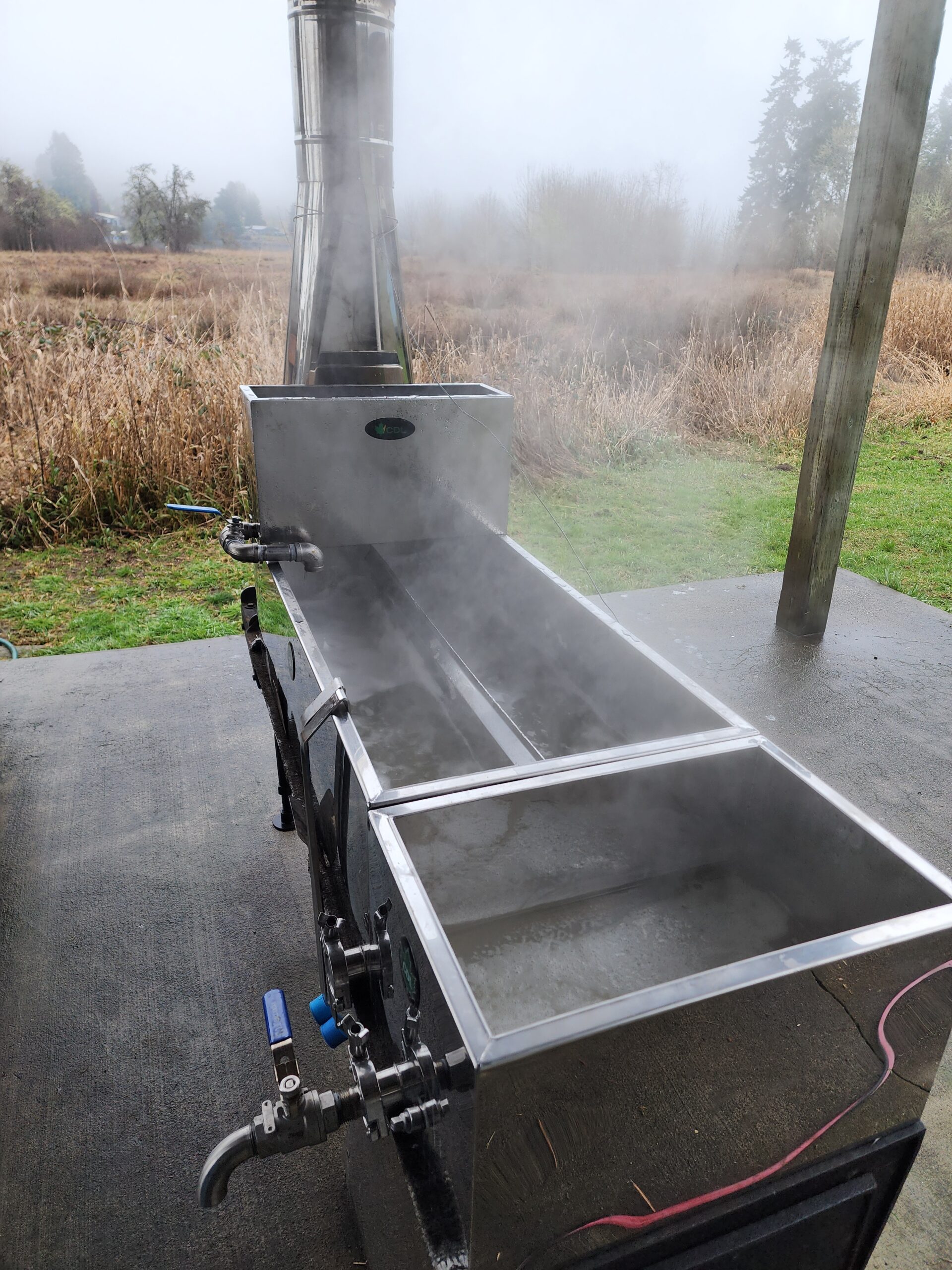 A stainless steel maple sap evaporator with steam rising from it.