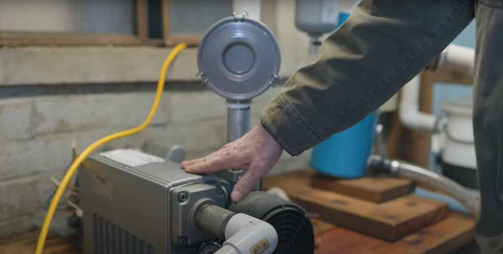 Neil placing his hand on a metal vacuum pump used to extract maple sap.