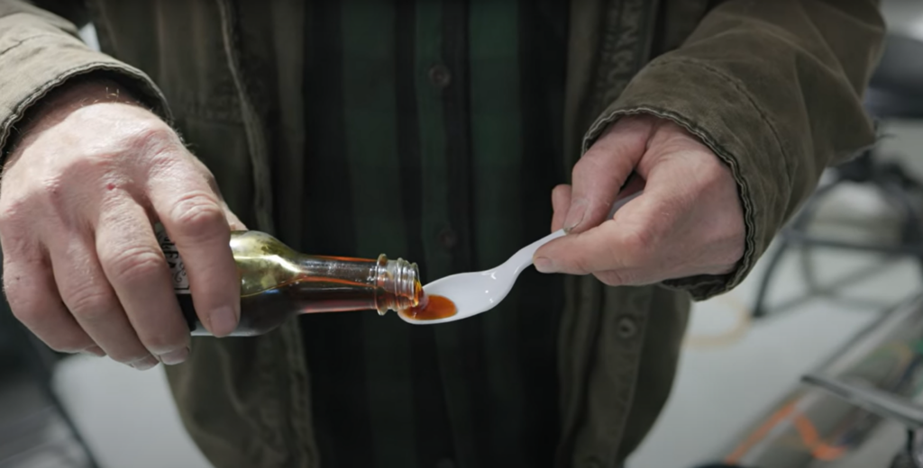 Neil pours out a small sample of maple syrup from a bottle into a plastic spoon. 