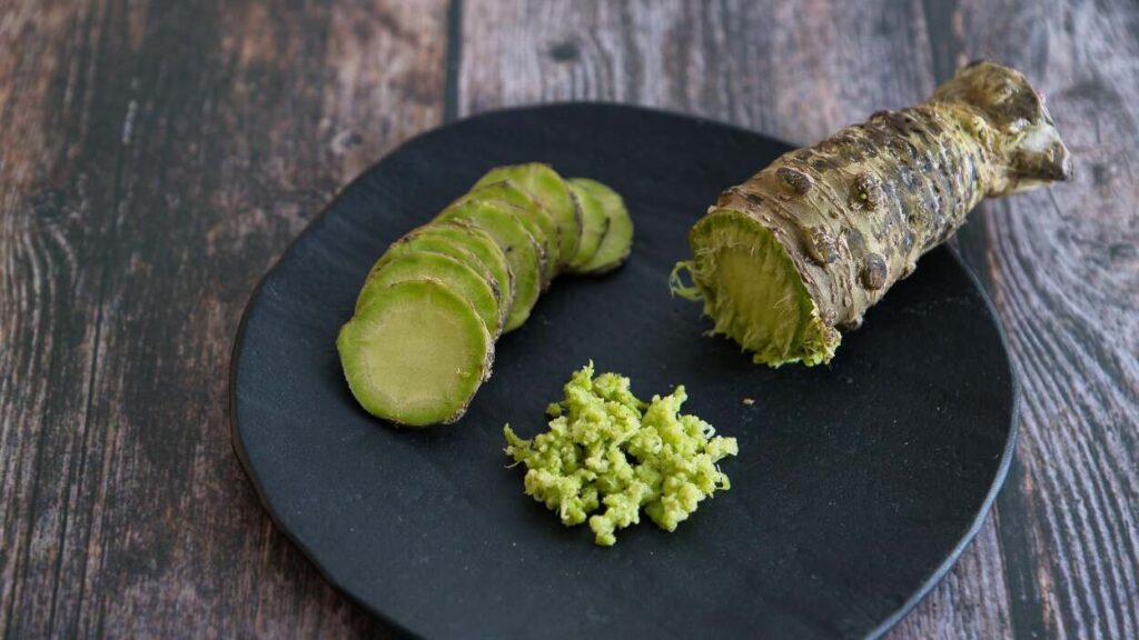 A wasabi stem on a plate next to wasabi that has been ground and sliced.