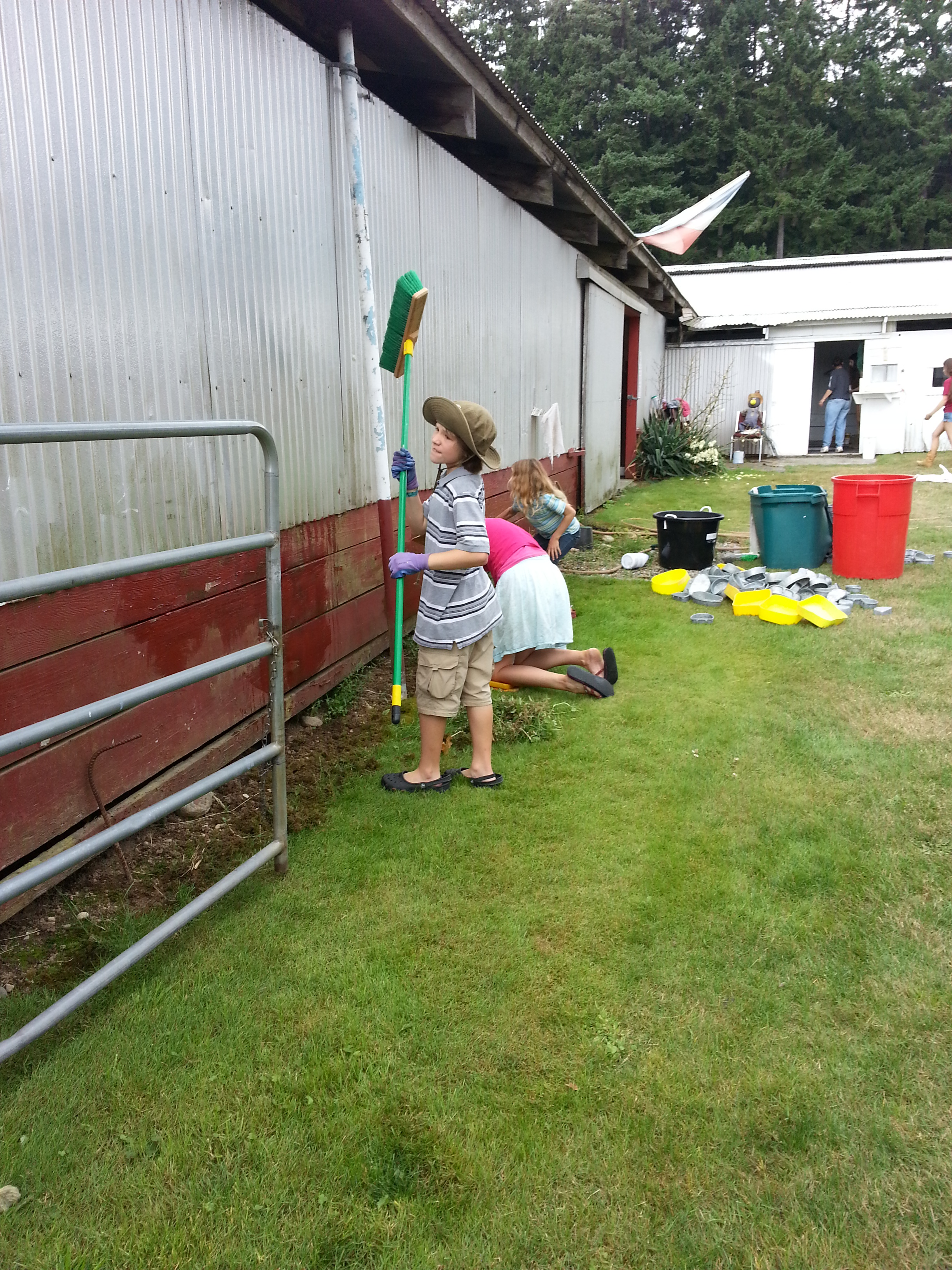 A youth washing the side of a building with a large broom. 
