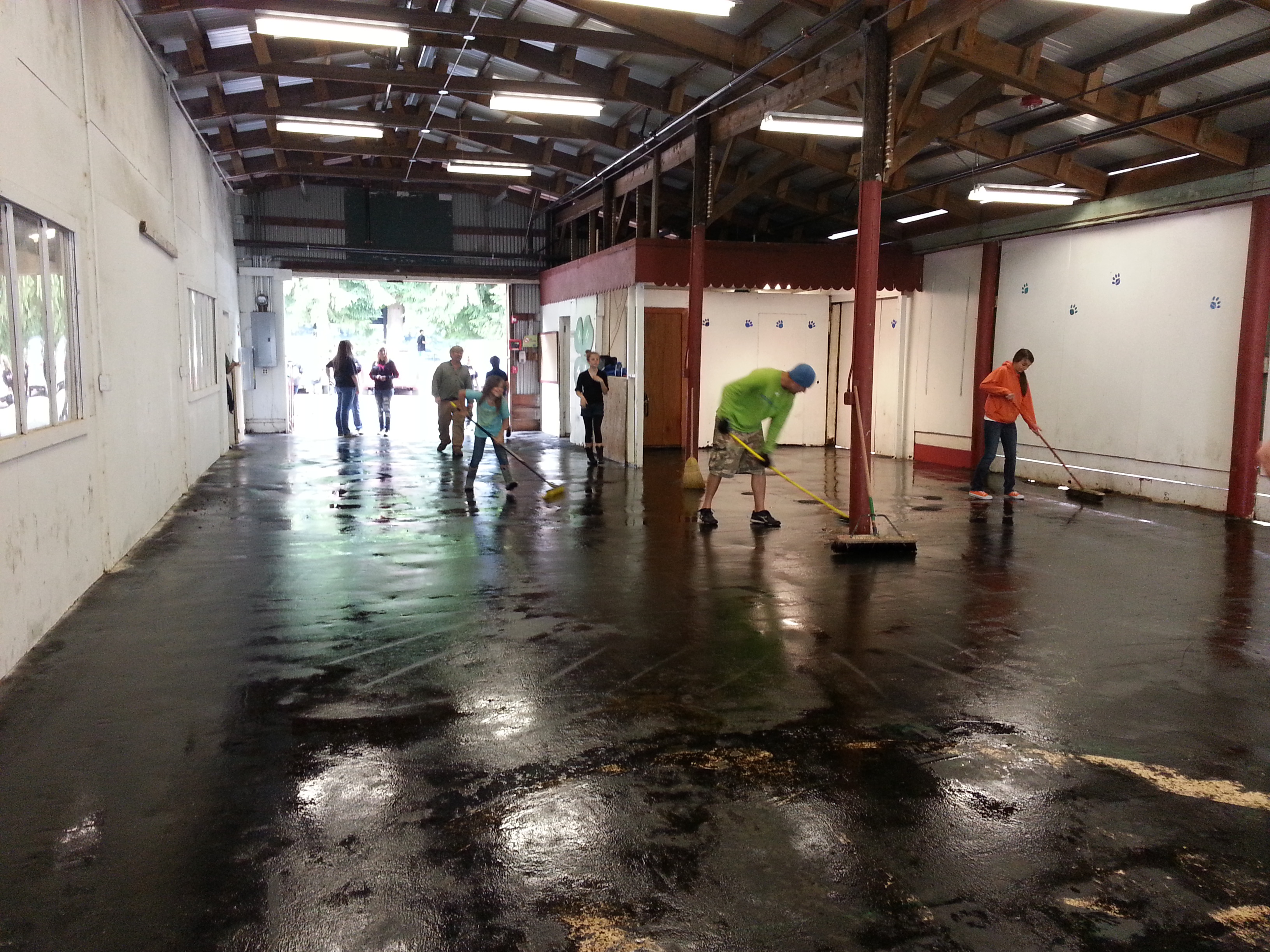 Many youth and adults mopping floors in a barn. 