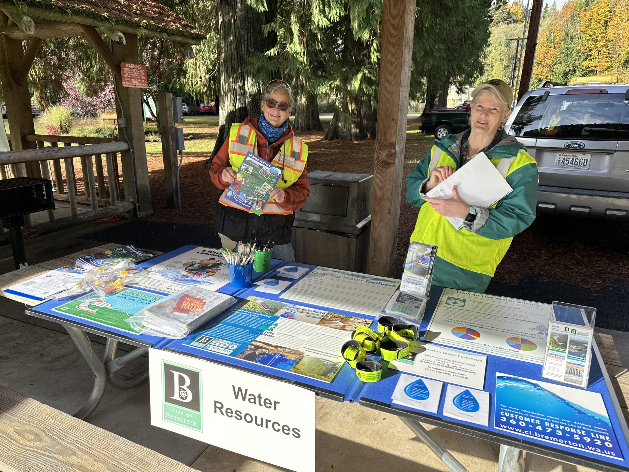 Photo of two City of Bremerton employees hosting a water resources table at Otto Jarstad Park for Salmon Tours event, providing resources about drinking water.