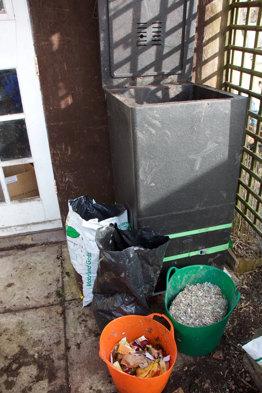 Black square plastic insulated composting box located outside of house door. 