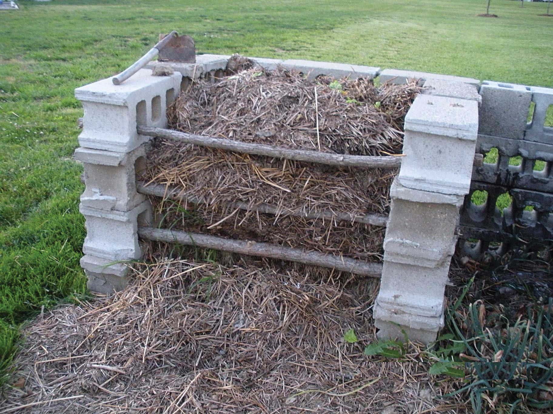 Compost bin made from cinder blocks, full of compost, and several branches used as gate to hold the compost in.