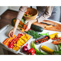 Person layering cut vegetables on baking tray. 