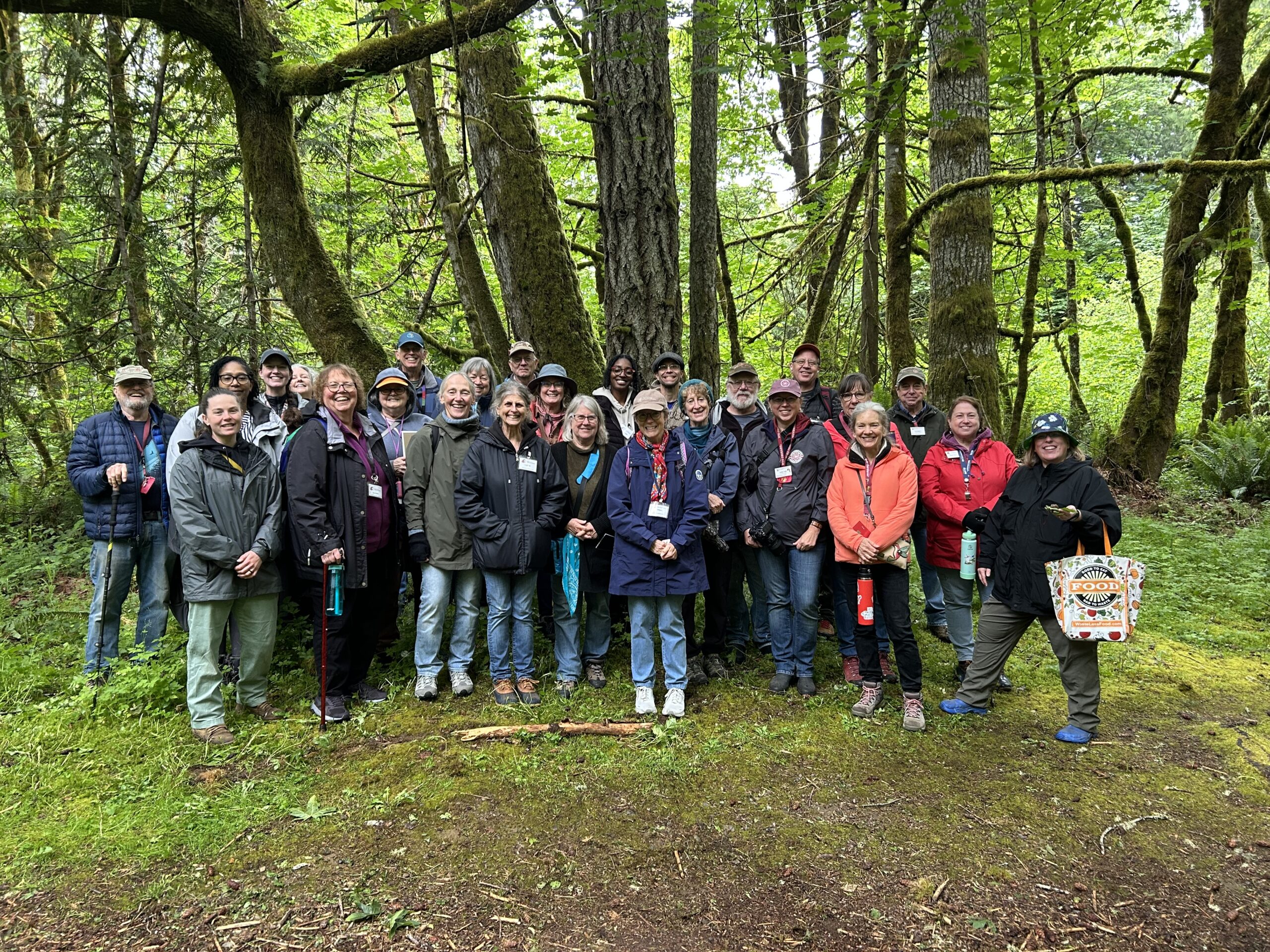 Thirty WSU Master Gardener trainees, mentors, and staff smiling for photo in front of trees on a trail.