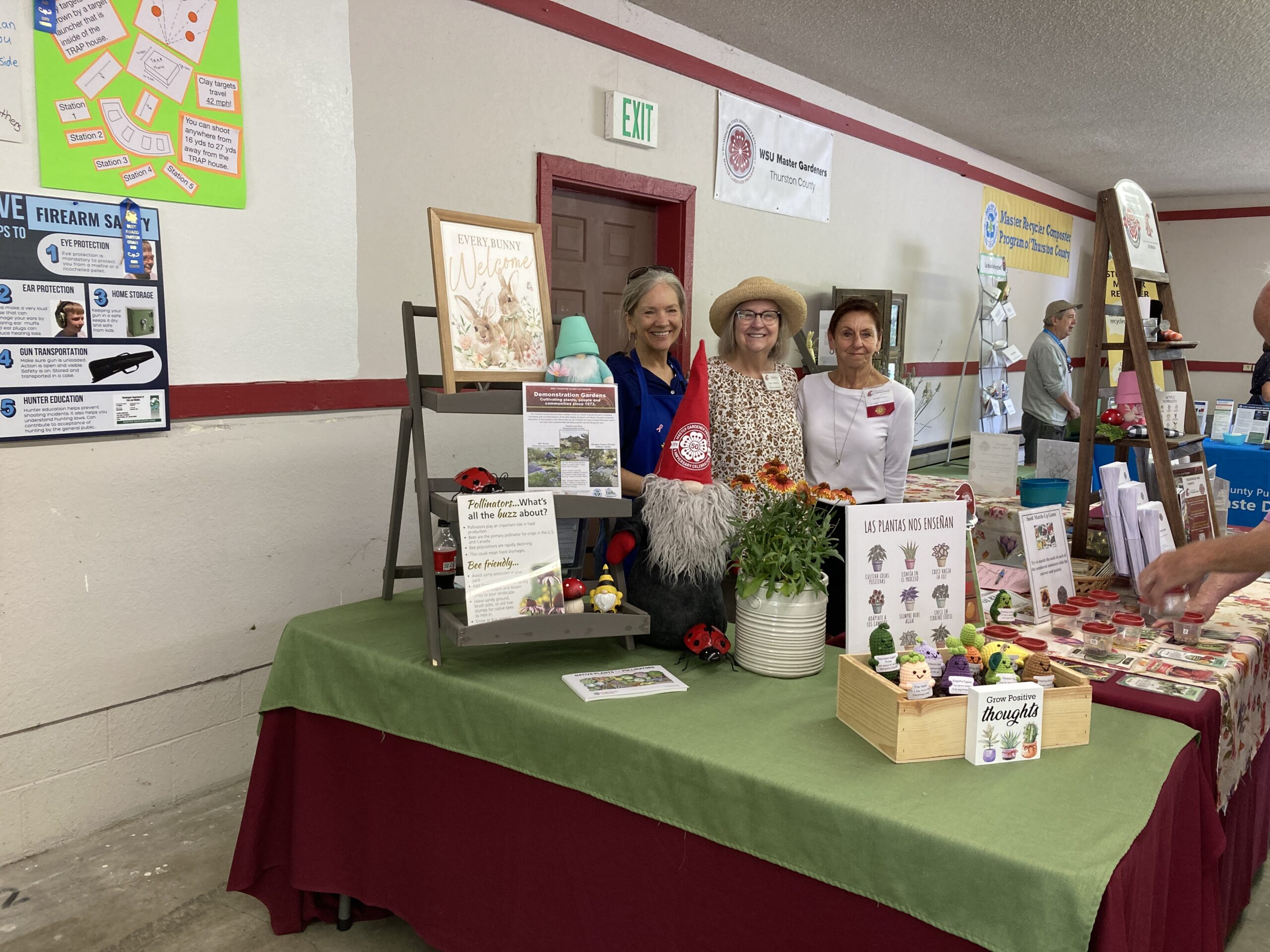 Three WSU Master Gardener volunteers smiling behind an information table with program information and decorations.
