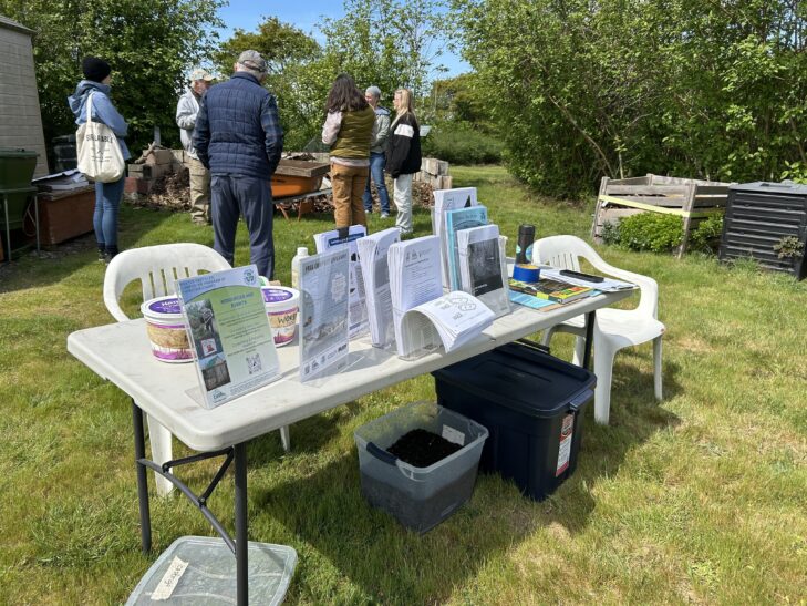 Volunteer teaching worm composting to group of people at Closed Loop Park Demonstration Garden. Table of workshop information in foreground.