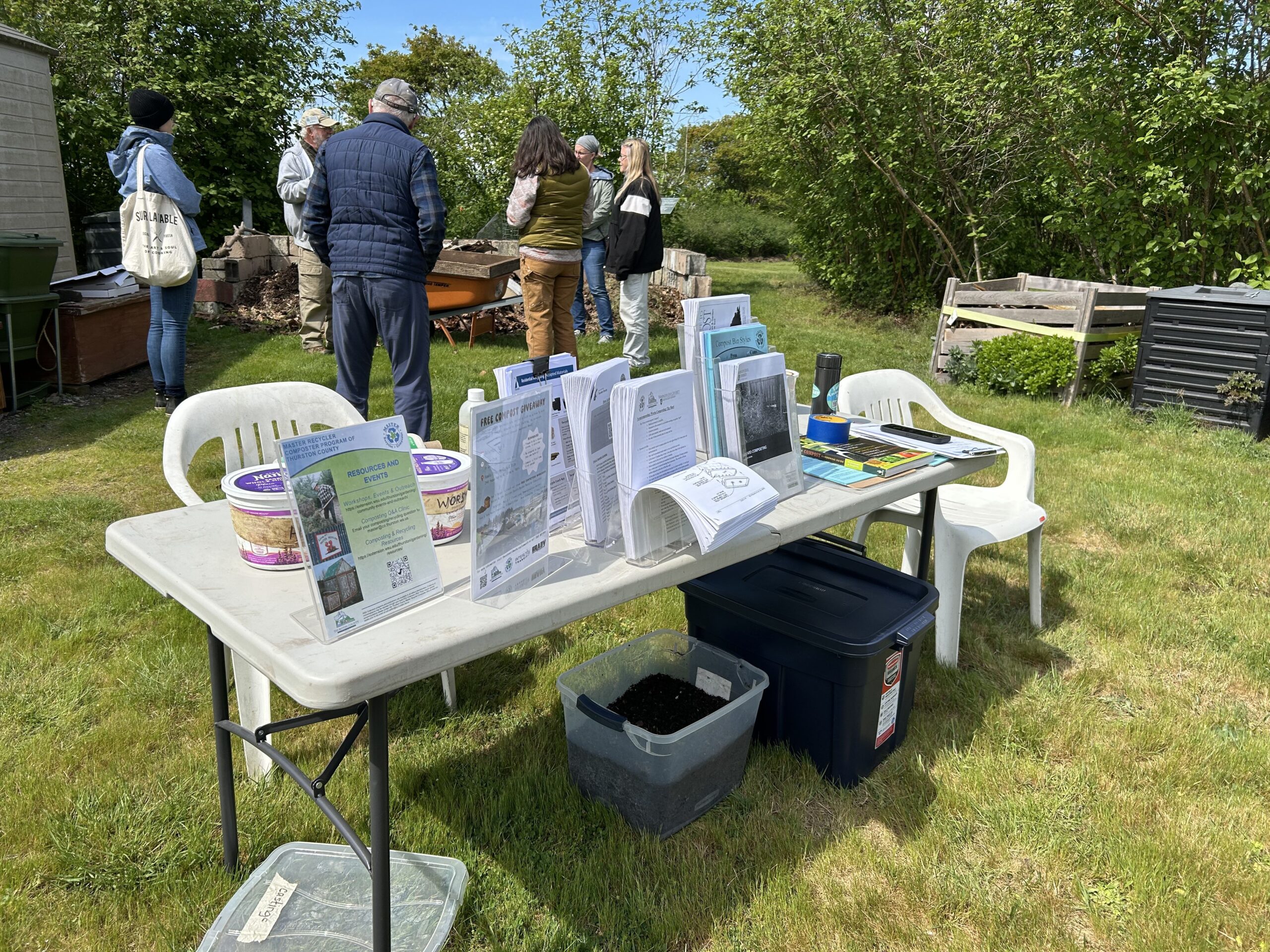 Volunteer teaching worm composting to group of people at Closed Loop Park Demonstration Garden. Table of workshop information in foreground.