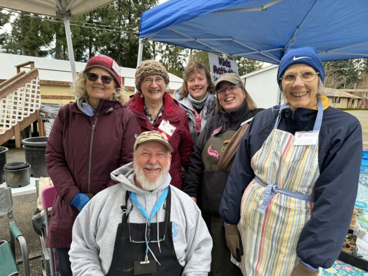 Master Gardener and Master Recycler Composter volunteers smiling in front of outreach booths.