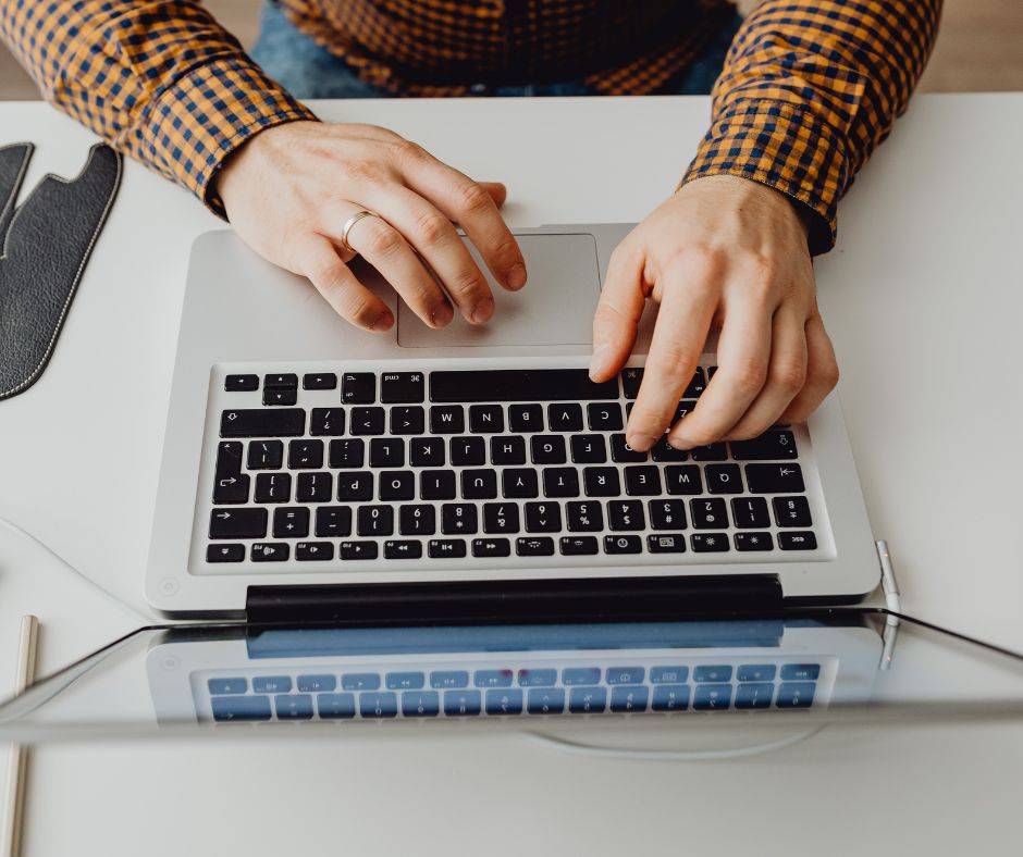 Person's hands typing on a laptop computer on a desk. 