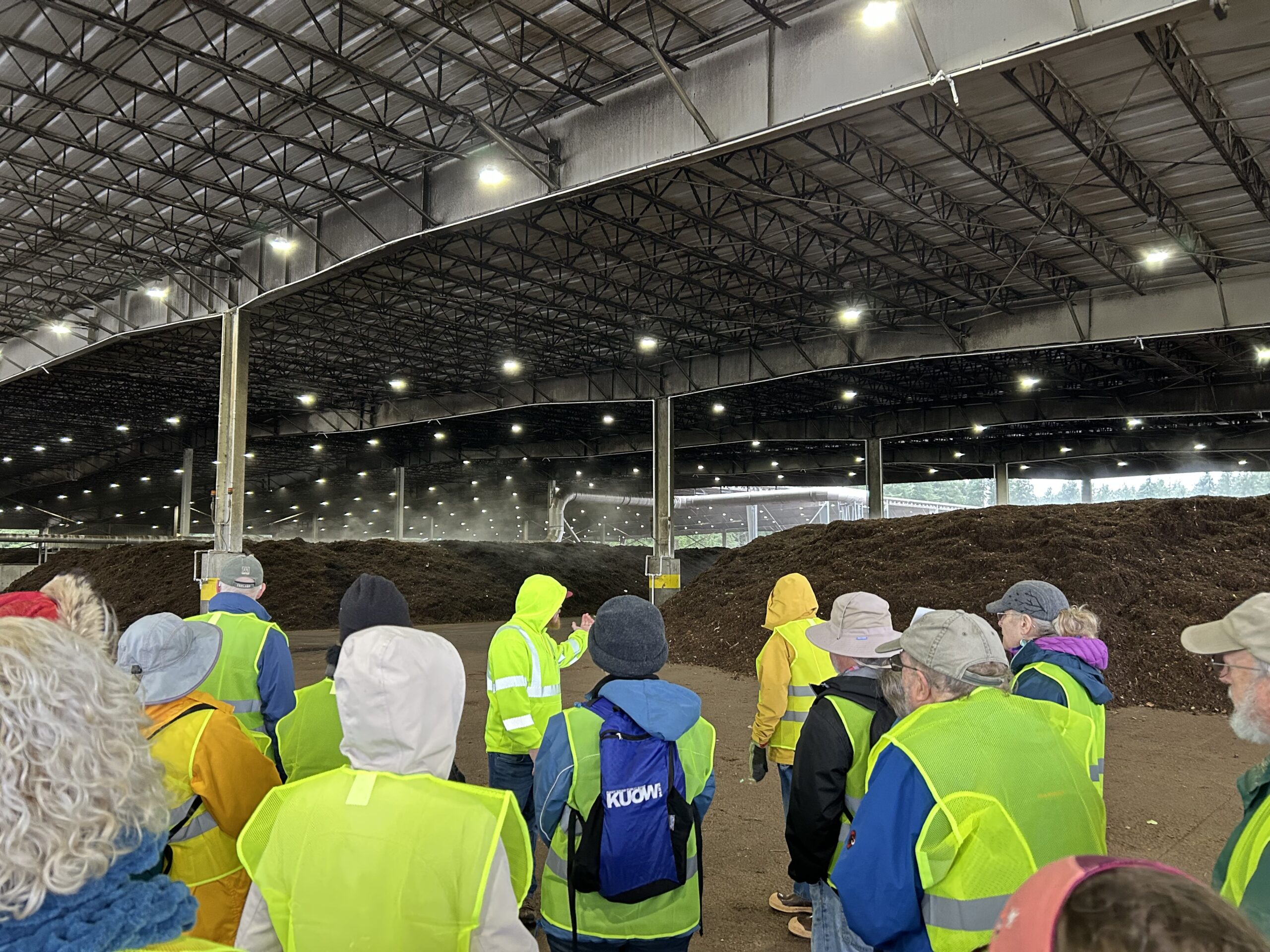 Group of trainees listening to compost facility worker talk about composting process. 