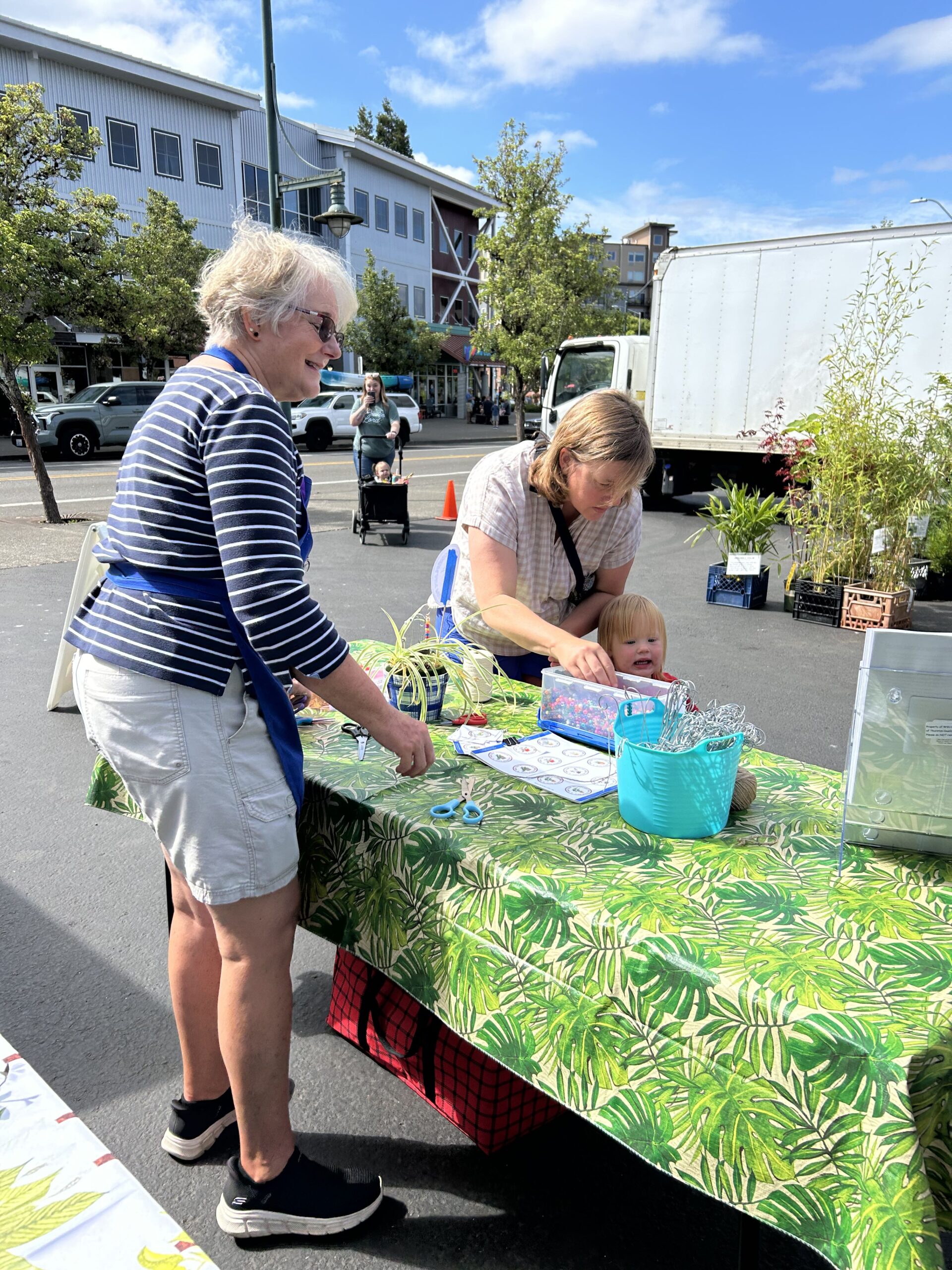Mom and child selecting decorations for houseplant at table with volunteer looking on. 