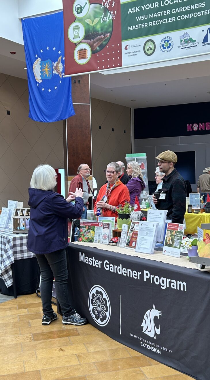 Two Master Gardener volunteers behind the outreach booth talking to a person.