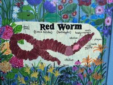 Painted mural of a red worm surrounded by painted flowers. 
