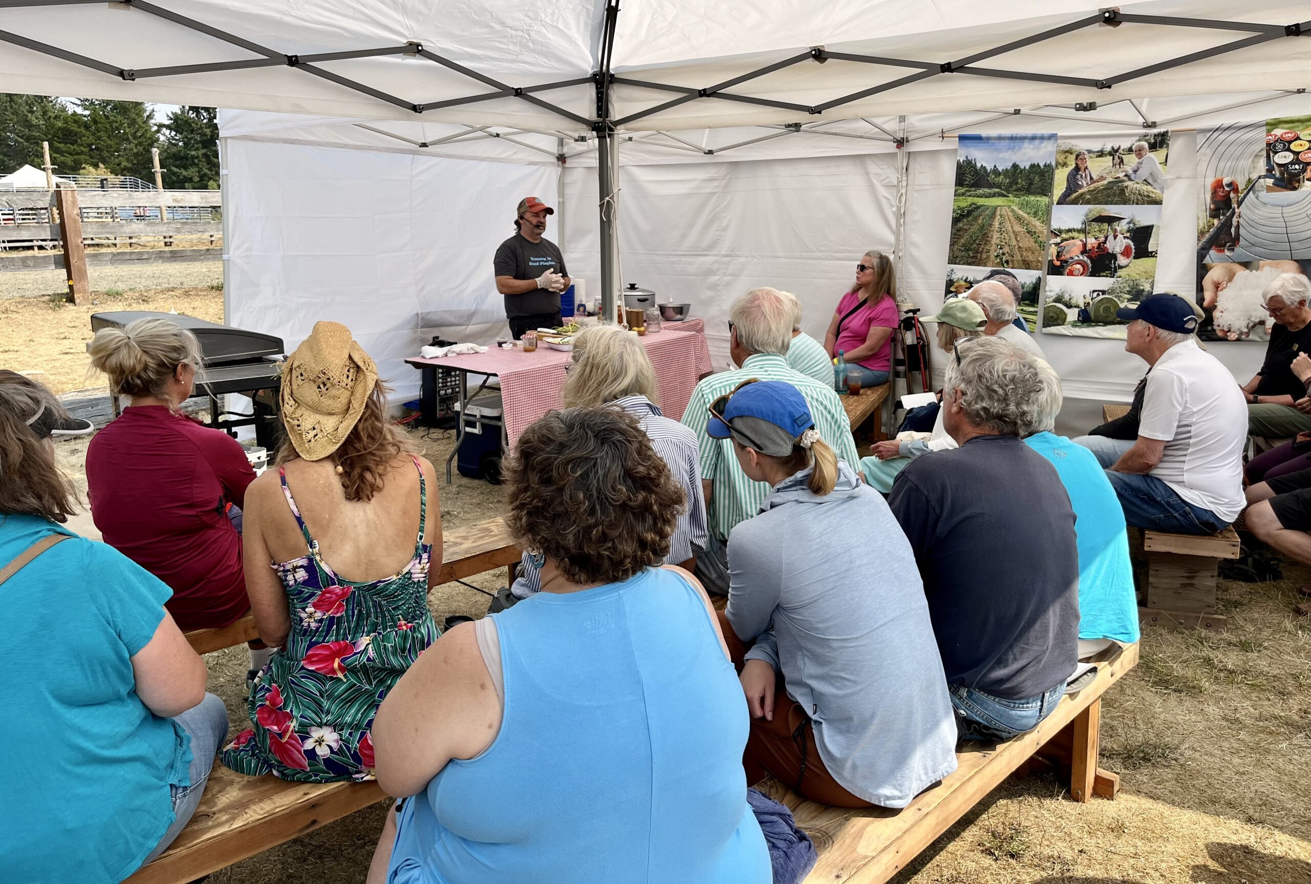 Photo of a Local Foods cooking demo at the San Juan County Fair with a local chef presenting to a group of fairgoers under a white tent and with colorful farm photo banners in the background.