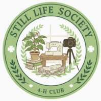 Circular logo for "Still Life Society 4-H Club." Features a potted plant, vintage sewing machine, and tripod camera, surrounded by laurel branches, with a dark green and gold border.
