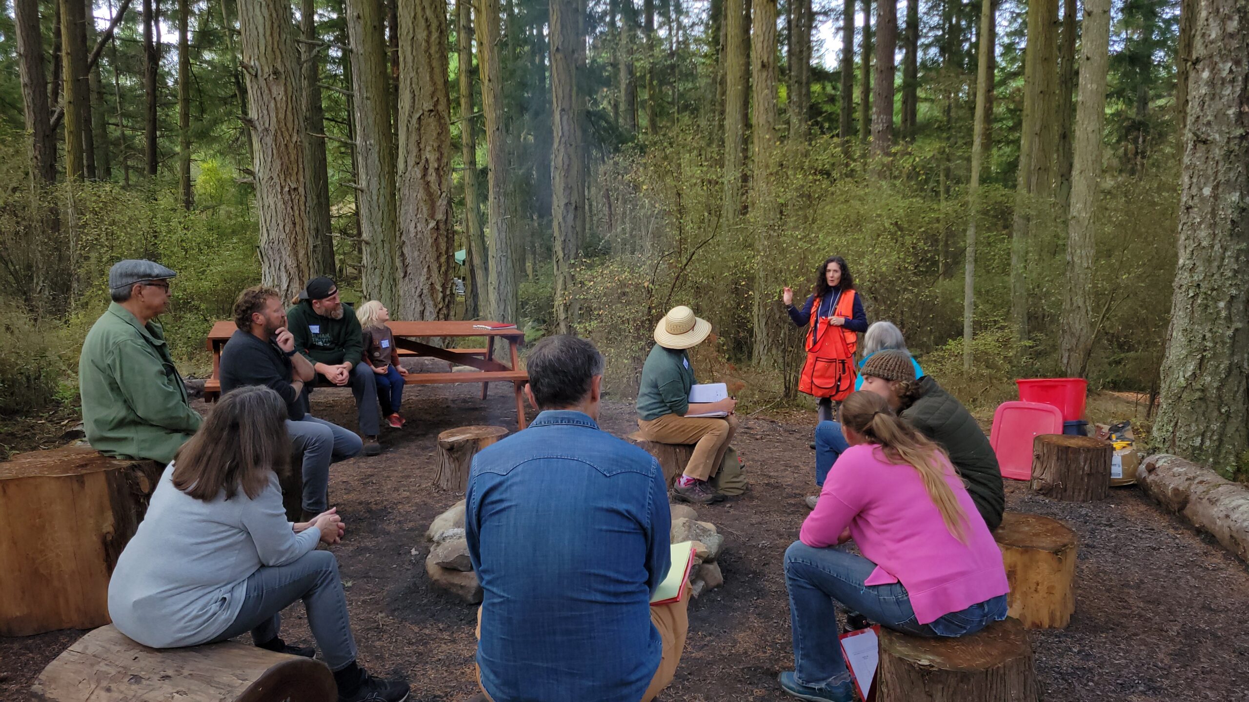 Group of people sitting in the forest listening to a presenter