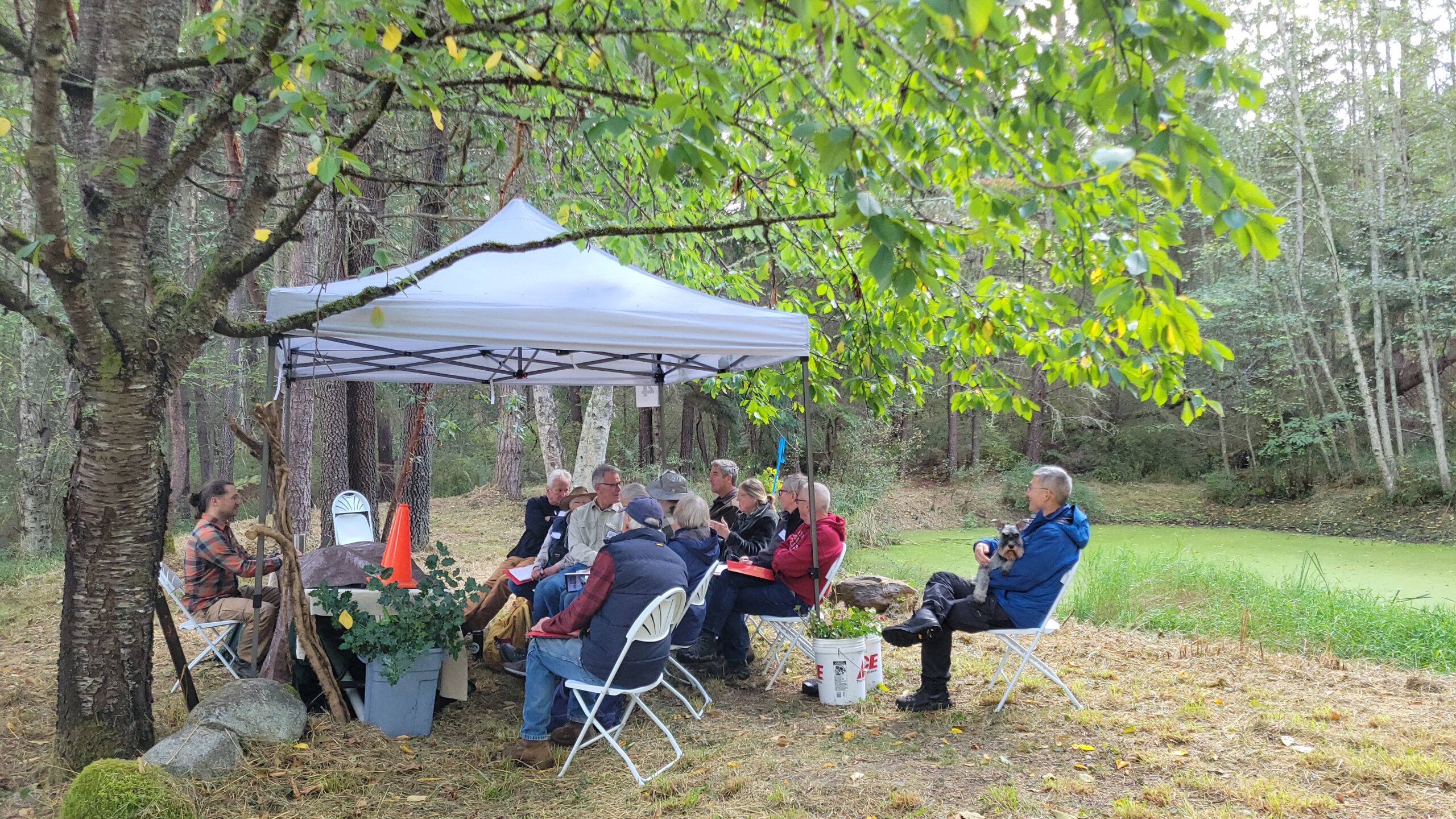 Group of people sitting under a tent listening to a presentation. 