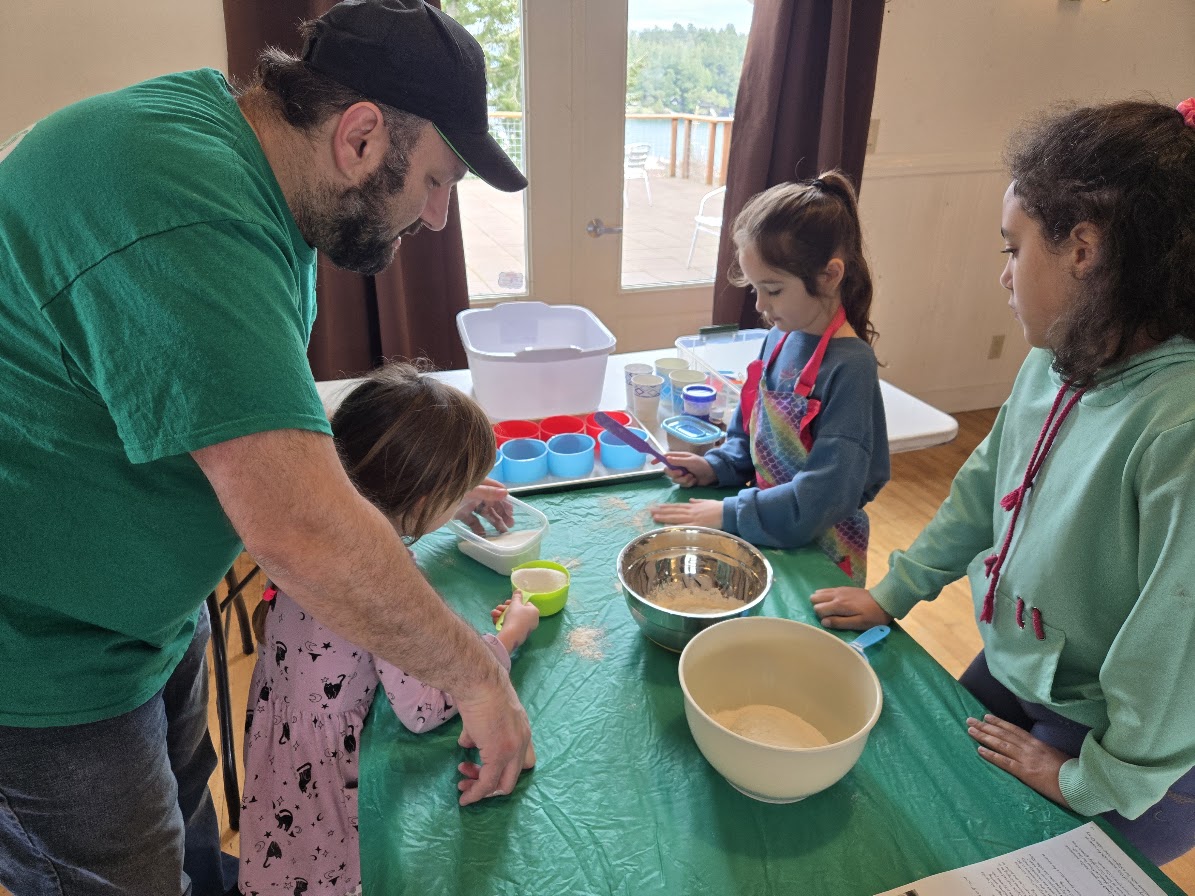 An adult helping young children measure ingredients during a baking activity indoors.