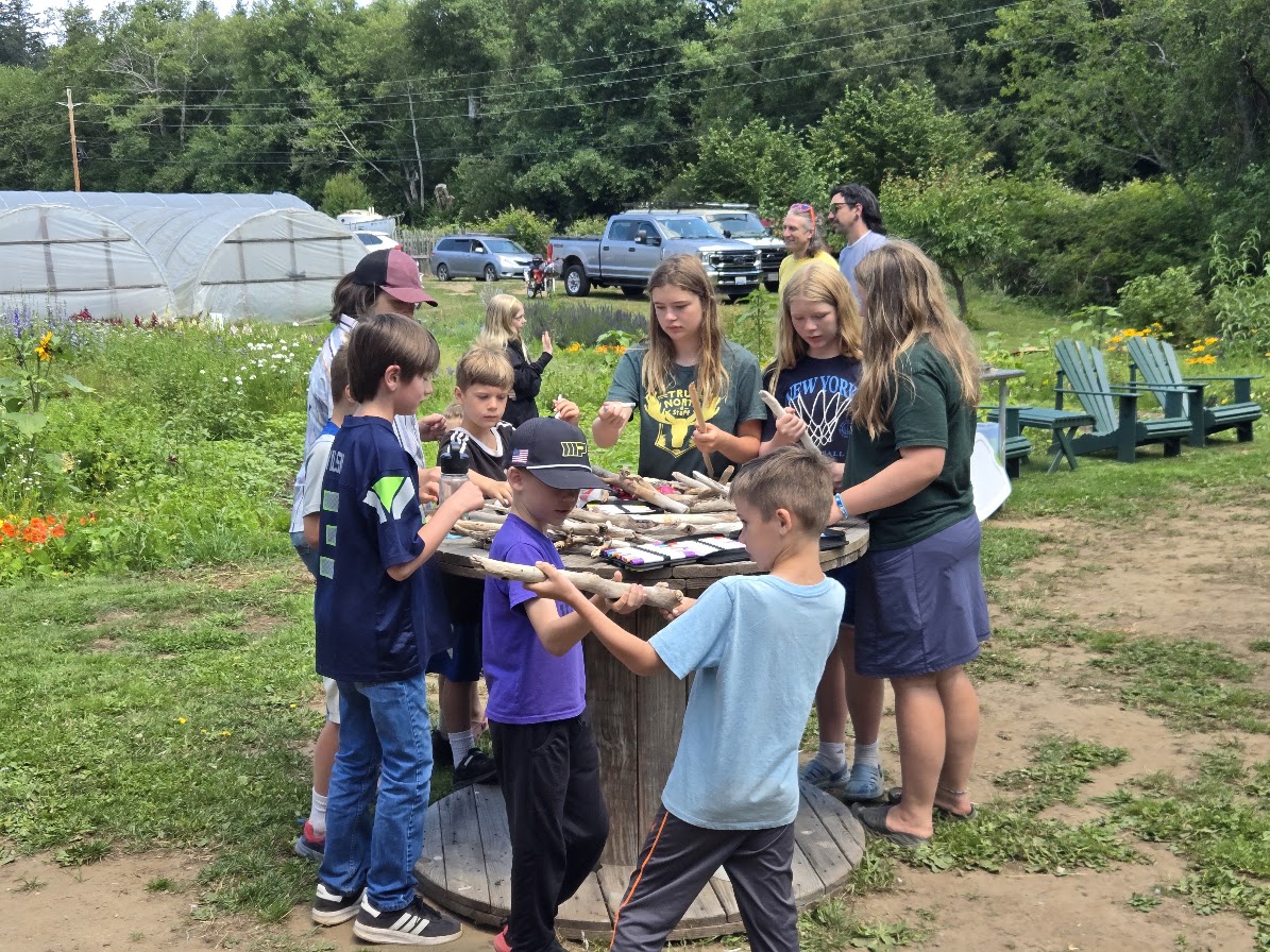 A group of adults and children gathered around tables indoors during a meeting or community activity.