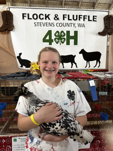 4-H girl holding her chicken in front of a 4-H display banner at the fair