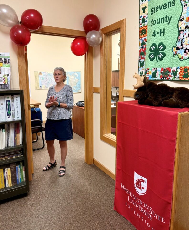 Debra Hansen standing in the door of her office on her last day.  Balloons in WSU colors are attached to the doorway.